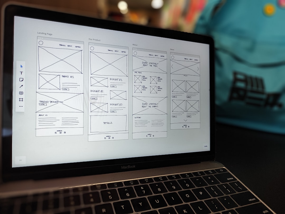 A website wireframe displayed on a MacBook screen sitting on an office desk.